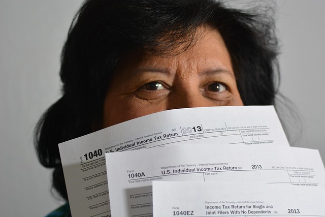 Concerned woman holding tax forms in front of her face.